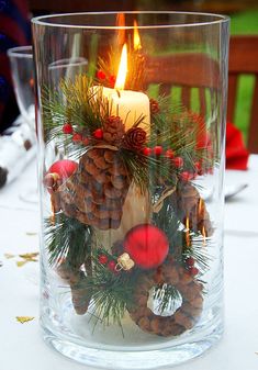 a candle that is sitting inside of a glass vase filled with pine cones and ornaments