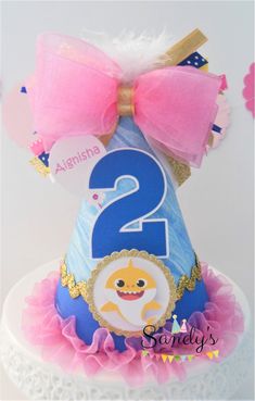 a blue and pink birthday hat with a number two on it's top, sitting on a lace doily