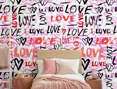 a bed sitting under a pink wall with lots of love written on the wall next to it