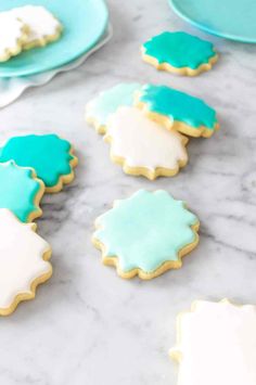 cookies decorated with blue and white icing on a marble countertop next to plates