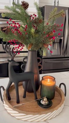 a candle and some decorations on a tray in the kitchen with pine cones, red berries and evergreen branches