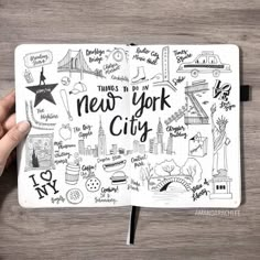 someone's hand holding a notebook with new york city doodles on it