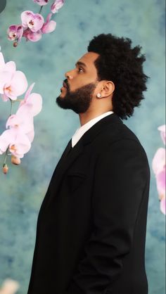 a man with long hair and beard standing in front of pink orchids on a blue background