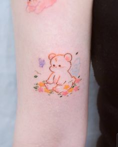 a small teddy bear tattoo on the left inner arm, with flowers and butterflies around it