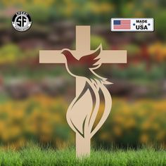 a cross with a bird on it in front of some grass and flowers, the words made in usa