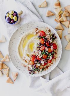 a bowl of hummus, olives and tomatoes with pita chips on the side