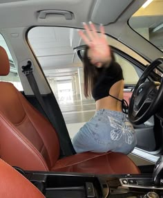 a woman is sitting in the driver's seat of a car and waving her hand