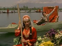 a woman in a red dress is sitting on a boat with flowers and other people