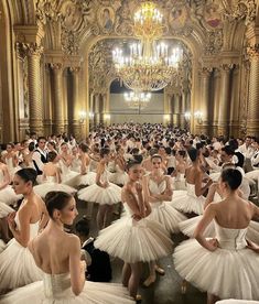 a large group of ballerinas in white tutus and dresses with chandeliers hanging from the ceiling