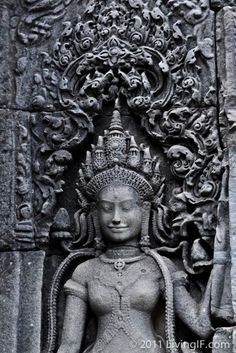 an intricately carved statue in front of a stone wall with carvings on the sides