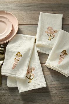 four white napkins with gold designs on them next to a pink plate and fork