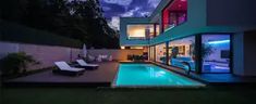 a house with a swimming pool and lounge chairs in the yard at night, lit up by colorful lights