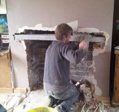 a man is working on a fireplace in his living room with the walls torn off