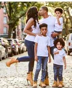 the family is posing for a photo on the cobblestone street in front of some parked cars