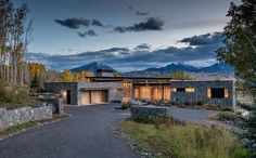 a large house with mountains in the background at dusk, surrounded by trees and shrubs