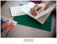 a person is cutting paper on top of a green table with scissors and other crafting supplies