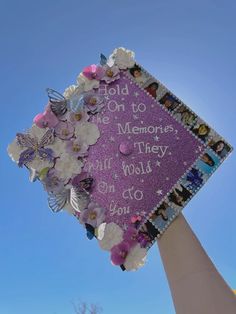 a purple graduation cap decorated with flowers and butterflies on top of a tall pole in front of a blue sky