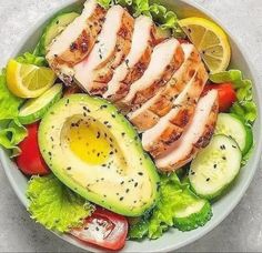 a salad with sliced chicken, avocado, tomatoes and cucumber slices