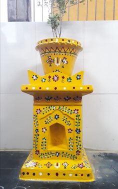 a yellow vase sitting on top of a black floor next to a planter filled with flowers