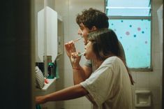 a young man and woman brushing their teeth in the bathroom while looking at each other