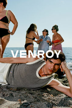 a man laying on top of a sandy beach next to the ocean with people standing around him