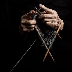 an old woman is knitting with her hands and holding the needles in front of her