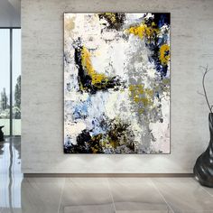 an abstract painting hangs on the wall next to a vase with yellow and blue flowers