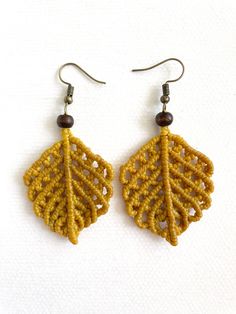 a pair of earrings made out of yellow thread and wood beads with leaves on them