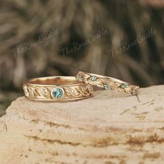 two gold wedding bands with green stones on top of a rock in front of a tree