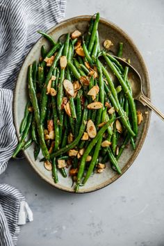 green beans with almonds in a bowl on a table next to a napkin and spoon