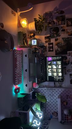 a computer desk topped with lots of clutter next to a wall covered in pictures