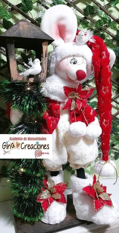 a white stuffed animal standing next to a christmas tree and birdhouse with red ribbon on it