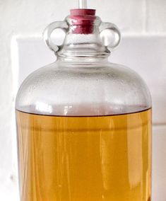 a glass jug filled with liquid sitting on top of a white tiled counter next to a wall