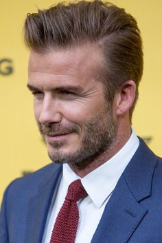 a man in a suit and tie smiling at the camera with a yellow wall behind him