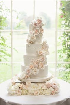 a three tiered wedding cake with flowers on the table in front of a window