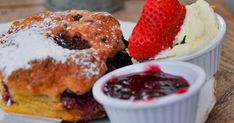 a strawberry and blueberry donut with powdered sugar on it next to a bowl of jelly