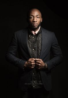 a man in a black suit and tie posing for a photo with his hands on his hips