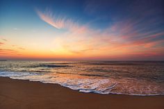 the sun is setting over the ocean with waves coming in to shore and some clouds