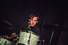 a man sitting behind a drum set in front of a black background with his hands on the drums