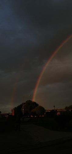 two rainbows are in the sky with dark clouds above them and houses on the other side