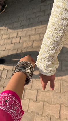 two people holding hands on a brick walkway with other people in the background and one person wearing bracelets