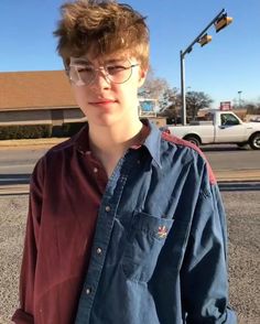 a young man wearing glasses standing in the street