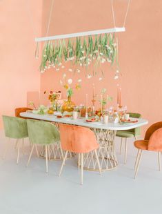 a dining room table set with green and orange chairs, flowers hanging from the ceiling