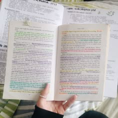 an open book in someone's hand on top of a bed