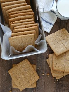 some crackers are in a tin on a table next to a glass of milk