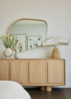 a white bed sitting under a large mirror next to a dresser with vases on it