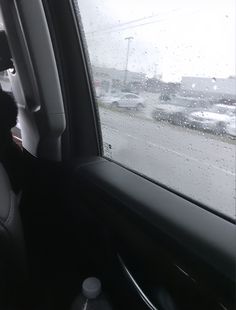 a black dog sitting in the passenger seat of a car on a rainy day with raindrops