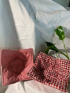 two red and white checkered cloths on a bed with a plant in the corner