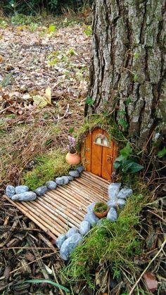 a small house made out of rocks and grass next to a tree in the woods