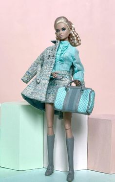 a barbie doll is holding a blue suitcase